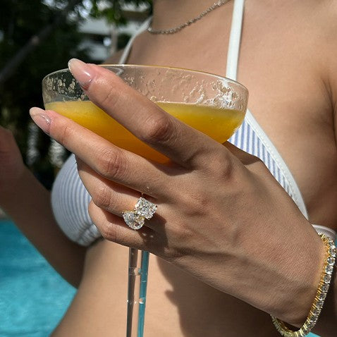 Hand with travel engagement ring holding a cocktail by the pool