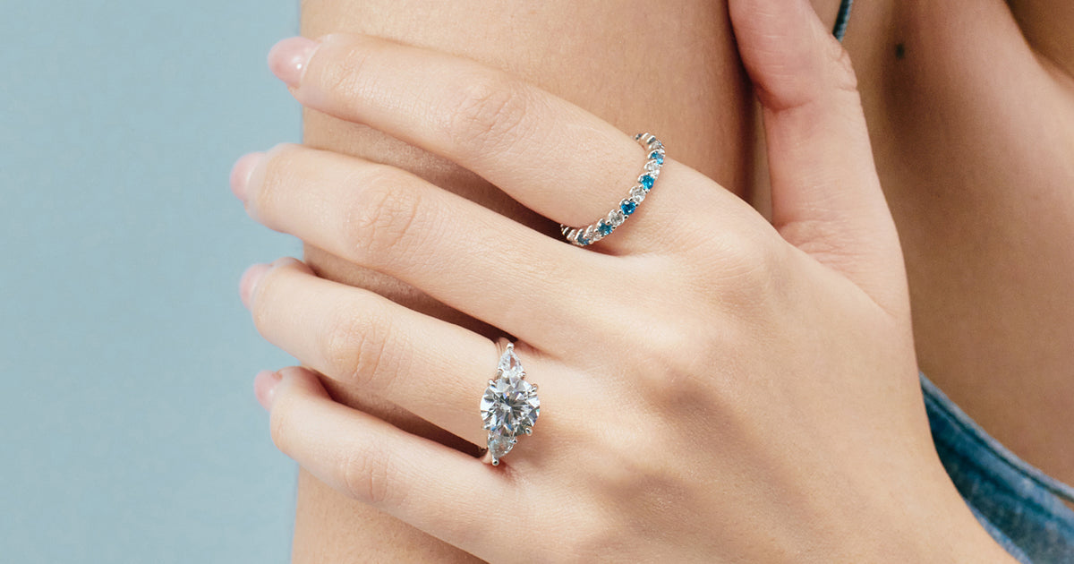 Hand wearing a blue topaz eternity band and a trilogy engagement ring