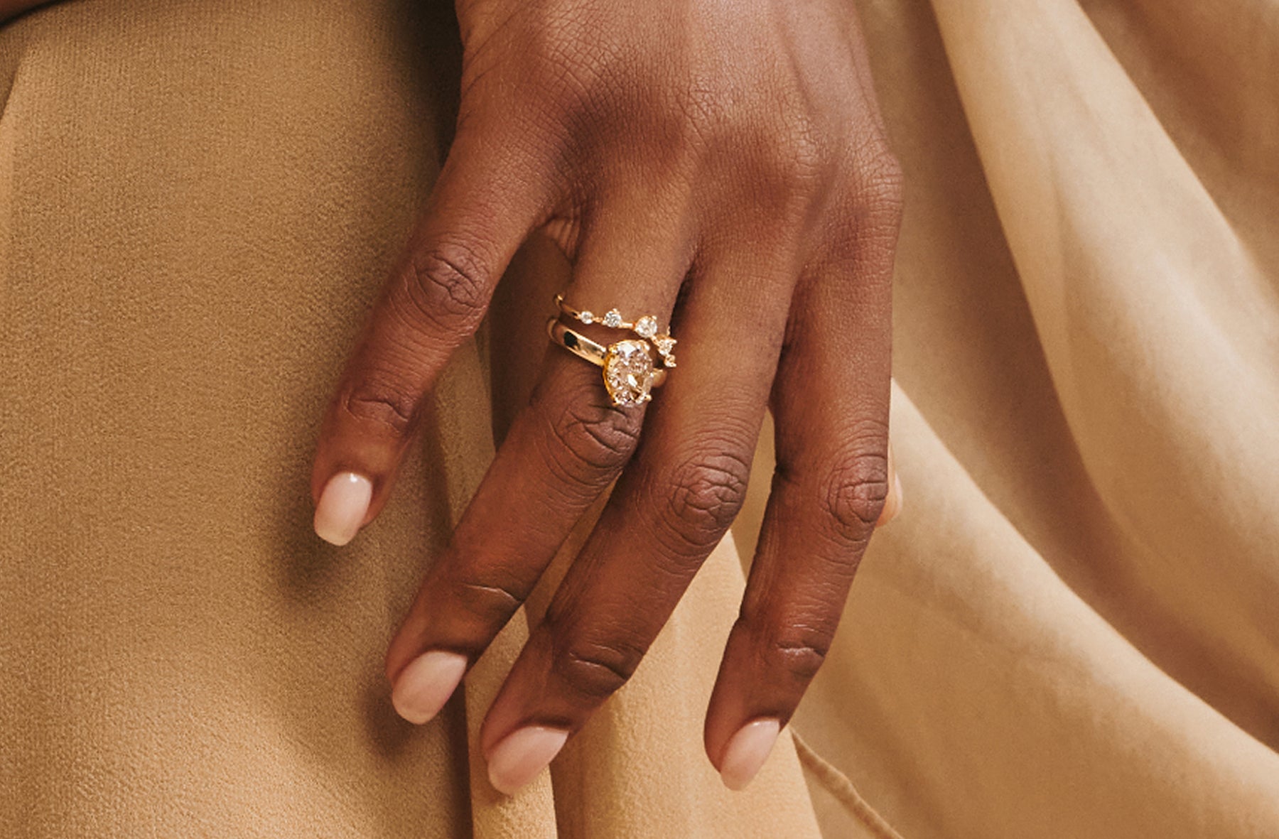 Hand wearing a gold ring stack resting on beige fabric