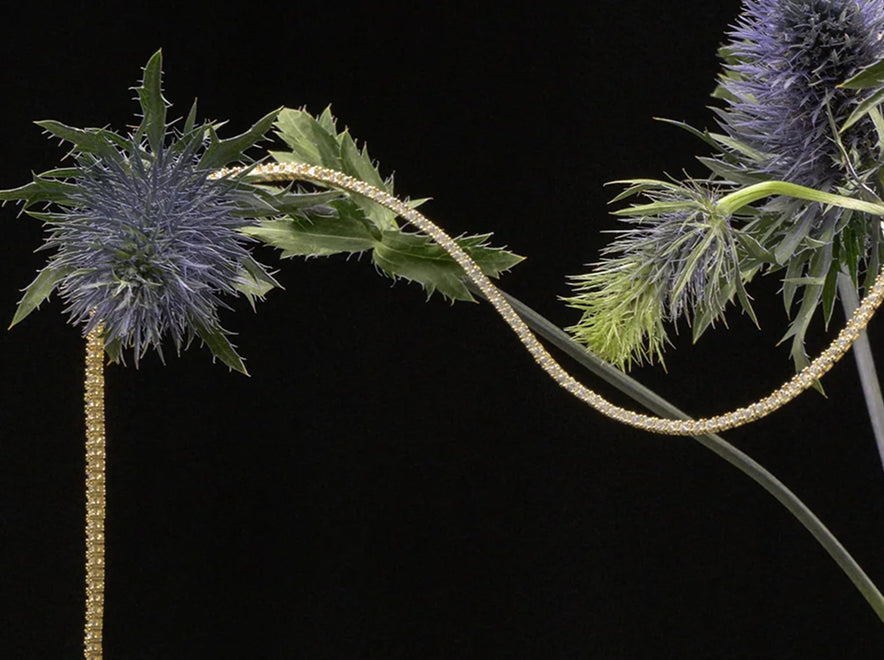 Gold tennis necklace draped over blue thistles