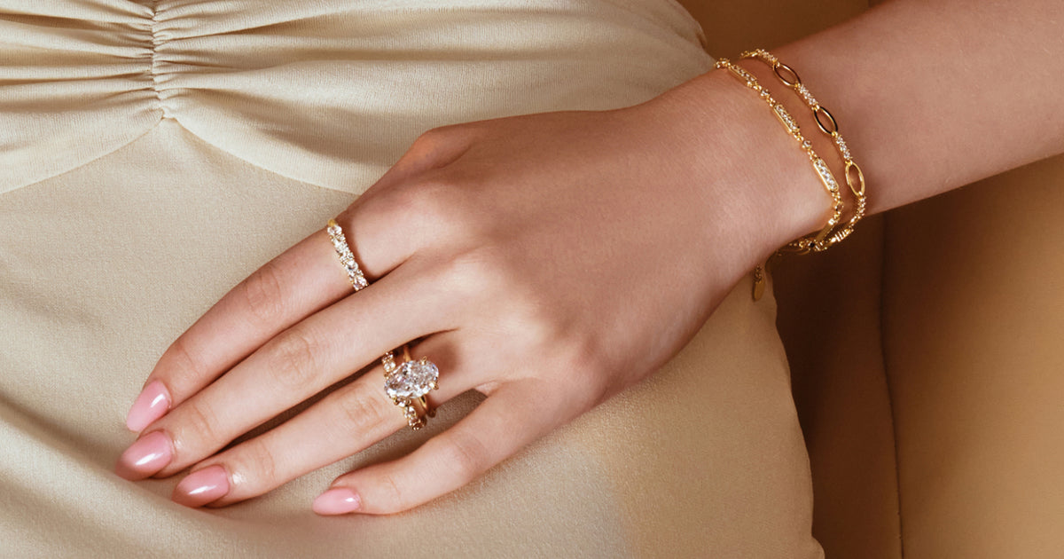 Hand wearing gold rings and bracelets against a champagne satin dress