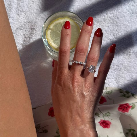 Hand with red nails wearing travel rings beside a glass of lemon water